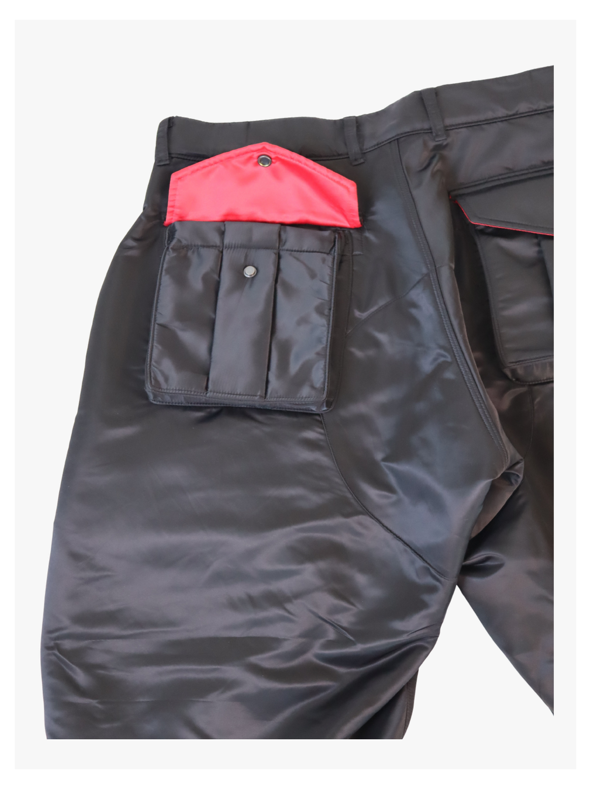 Close-up of red satin pocket flap on black utility pants by RCSLA, showcasing contrast stitching and snap button